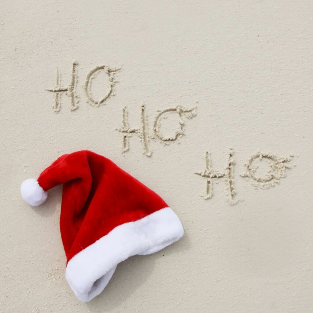 Ho Ho Ho written in the sand next to a santa hat